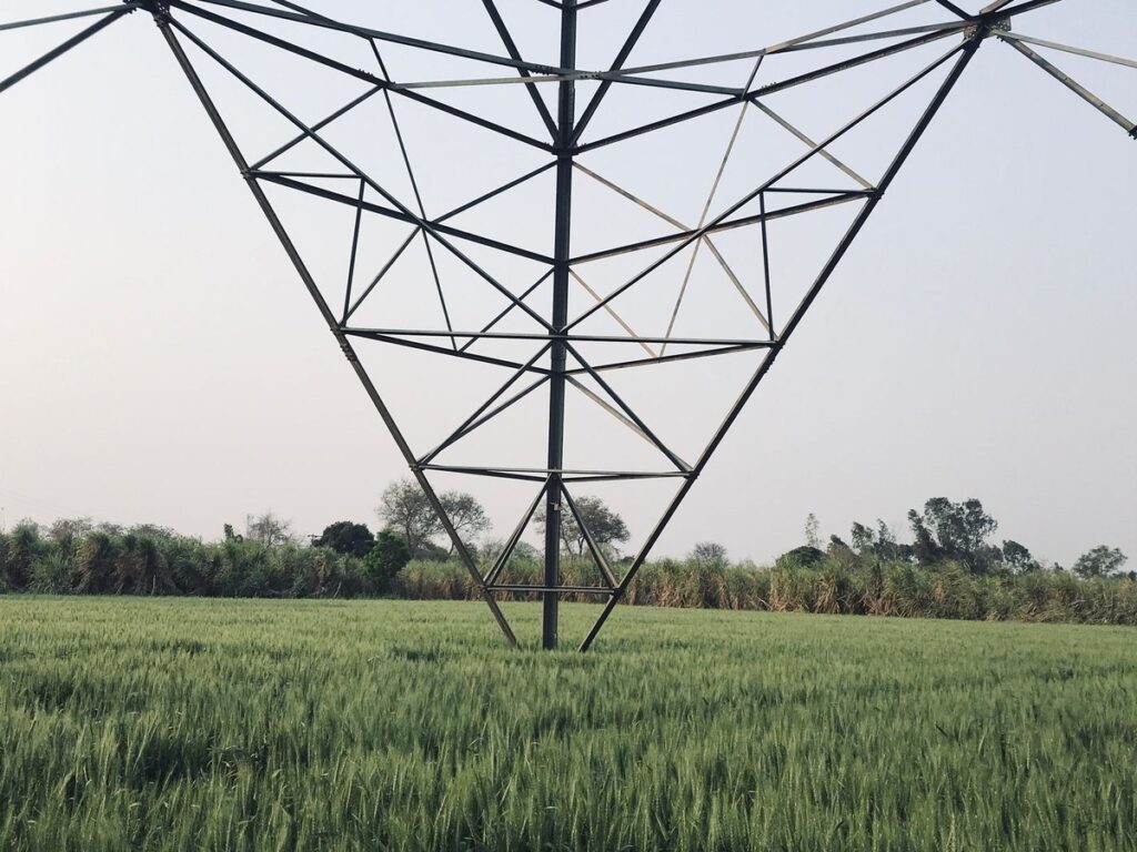 High-voltage transmission tower standing in a green field in rural India