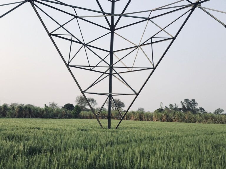 High-voltage transmission tower standing in a green field in rural India