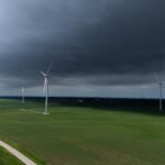 Wind turbines generating power across green fields under a stormy sky
